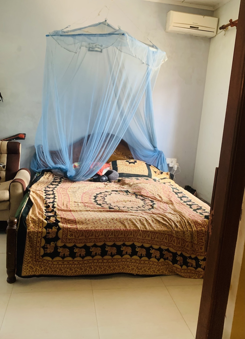 Quarto com cama queen-size. Uma cadeira da sala ao lado, um vento ao lado da cama com vista para o c ...