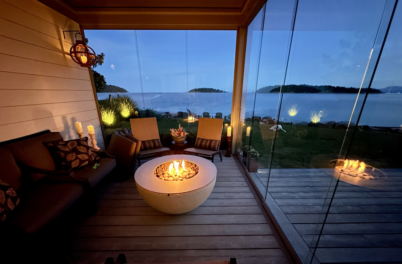 Covered seating area on the deck with a gas fire bowl and two glass walls that can slide open or clo ...