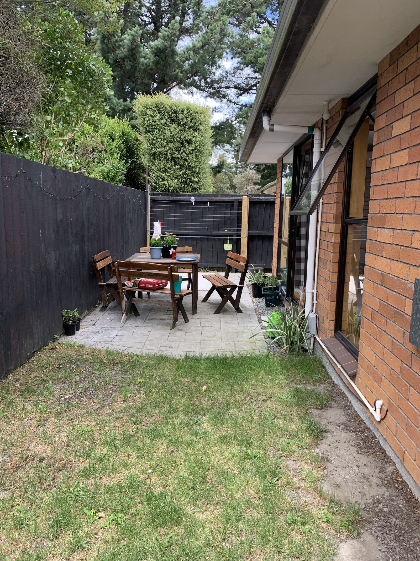 Private patio area partially grass and partially paved with outdoor table and chairs and clothesline ...